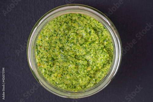 Green pesto sauce in a glass bowl isolated on black background, close up, top view