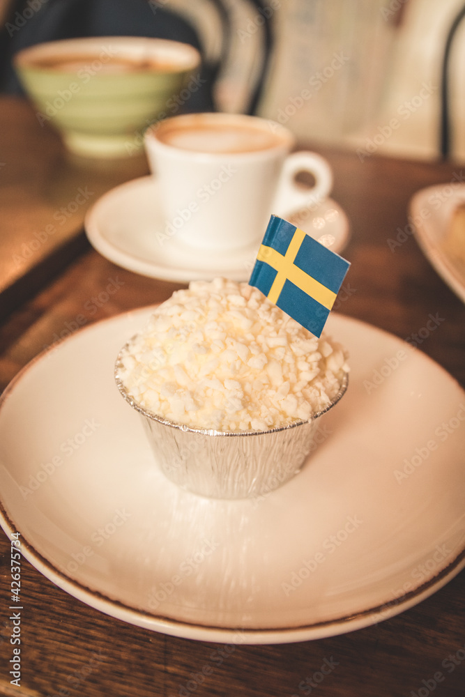 Traditional swedish cream cake with a cup of coffee on the back of a wooden table in a cute cafe. Swedish flags. Coffee break concept Traditional swedish cream cake with a cup of coffee on the back of a wooden table in a cute cafe. Swedish flags. Coffee break concept
