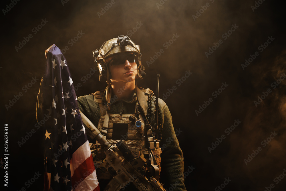 Special forces soldier holding US national flag in the dark Special forces soldier holding US national flag in the dark