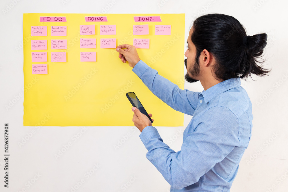 Business young man working on a scrum planning made on a yellow board on a white wall. Young man working on a project Business young man working on a scrum planning made on a yellow board on a white wall. Young man working on a project