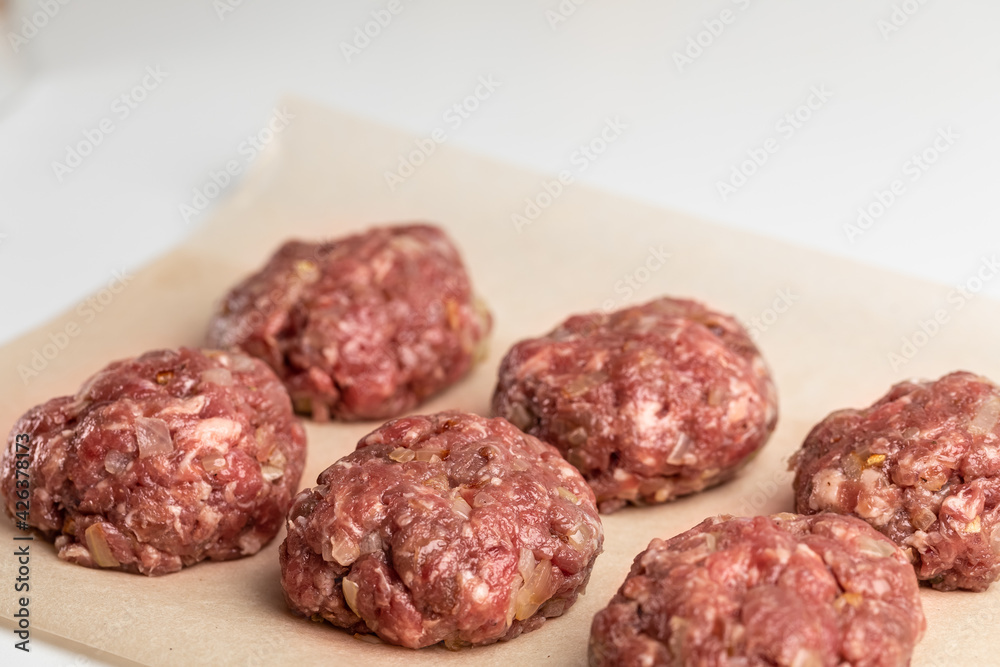 Raw unroasted beef cutlets on parchment paper. The process of cooking a non-vegetarian dinner. Place for the inscription Raw unroasted beef cutlets on parchment paper. The process of cooking a non-vegetarian dinner. Place for the inscription