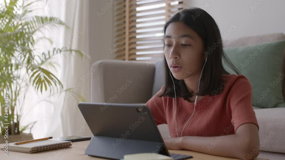 Asian girl learning online with tutor on tablet with headphones and talking Asian girl learning online with tutor on tablet with headphones and talking