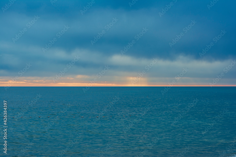blue sea and blue sky with bright streak of sunlight. sun rays passing through thick clouds