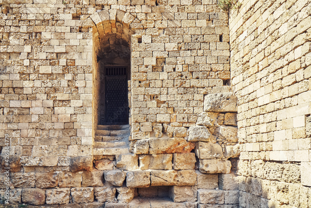Weathered ancient Rhodes fortress brick and stone wall with empty arch doorway under bright sunlight in summer Greece