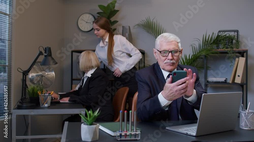 Senior professional businessman grandfather company director in modern office interior using mobile phone texing message working watching video successful people communicating. Elderly freelancer man photo