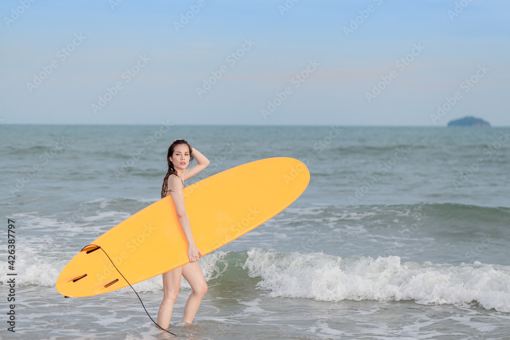 attractive sexy young asian woman surfer girl in bikini   poses on sandy beach with surfboard , water sports, healthy active lifestyle, summer vacation, extreme sport.