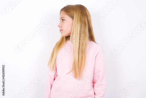 Side view of young happy smiling beautiful caucasian little girl wearing pink hoodie over white background