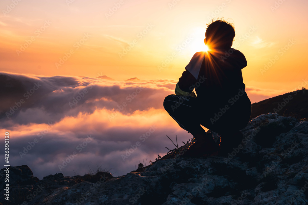 Niño senderista  disfrutando del atardecer en lo alto de la montaña.
Hiker boy enjoying the sunset at the top of the mountain.
 - obrazy, fototapety, plakaty 