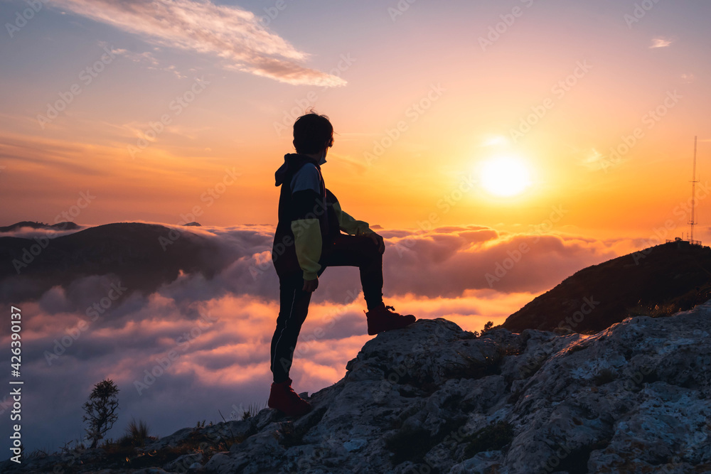 Niño senderista  disfrutando del atardecer en lo alto de la montaña.
Hiker boy enjoying the sunset at the top of the mountain.
