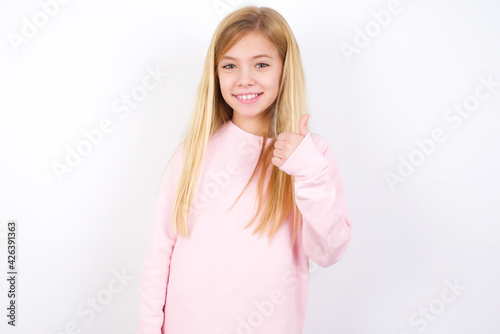 beautiful caucasian little girl wearing pink hoodie over white background giving thumb up gesture, good Job! Positive human emotion facial expression body language. © Jihan