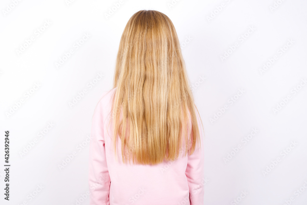 beautiful caucasian little girl wearing pink hoodie over white background standing backwards looking away with arms on body. beautiful caucasian little girl wearing pink hoodie over white background standing backwards looking away with arms on body.