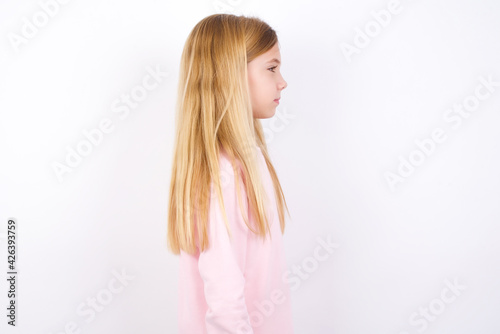 Profile of smiling beautiful caucasian little girl wearing pink hoodie over white background with healthy skin  has contemplative expression  ready to have outdoor walk.