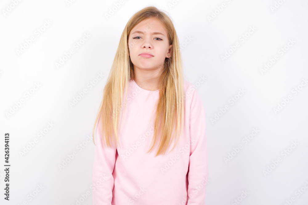 Gloomy, bored beautiful caucasian little girl wearing pink hoodie over white background frowns face looking up, being upset with so much talking hands down, feels tired and wants to leave. Gloomy, bored beautiful caucasian little girl wearing pink hoodie over white background frowns face looking up, being upset with so much talking hands down, feels tired and wants to leave.