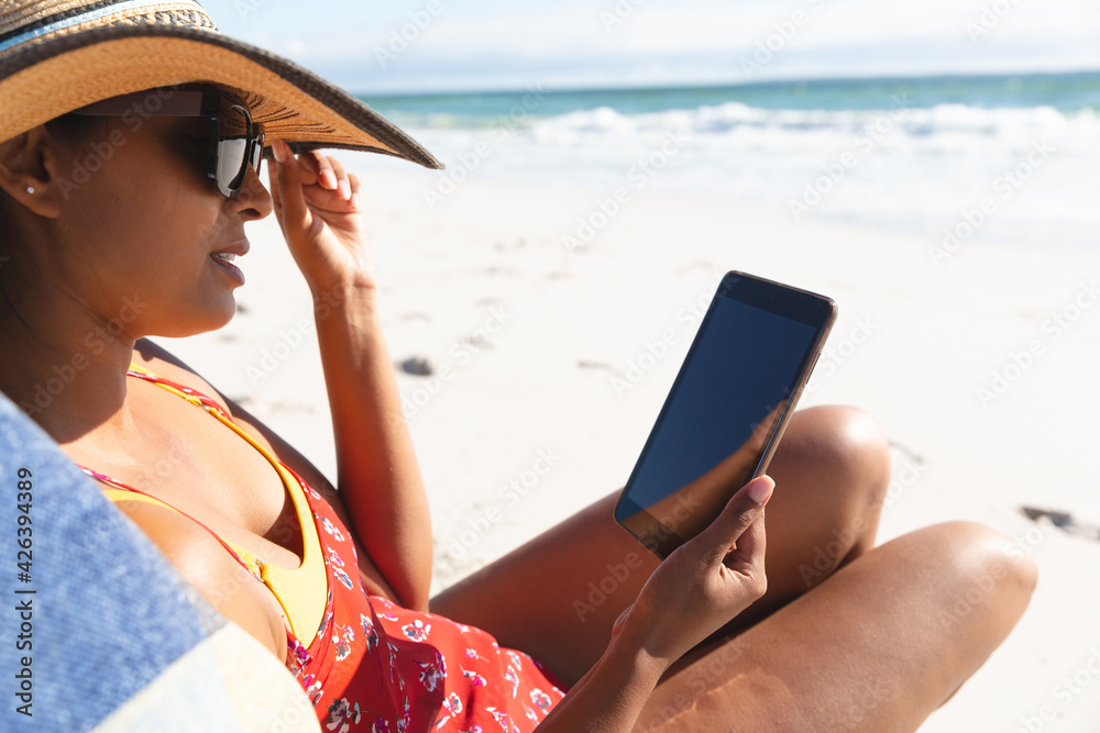 Mixed race woman on beach holiday sitting in deckchair using tablet