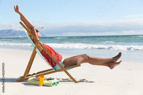 Mixed race happy woman on beach holiday sitting in deckchair stretching