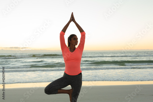 Mixed race woman on beach practicing yoga at sunset