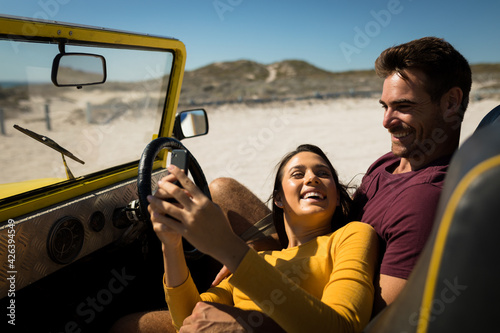 Caucasian couple lying on a beach buggy by the sea using smartphone