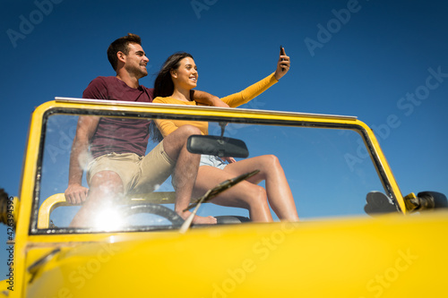 Happy caucasian couple sitting in beach buggy by the sea taking selfie