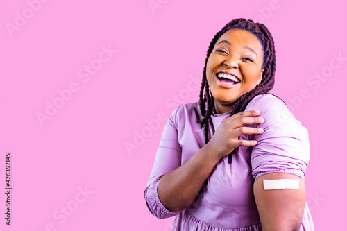 People healthcare and protection concept positive woman getting vaccination and showing a hand with plaster in pink studio photo