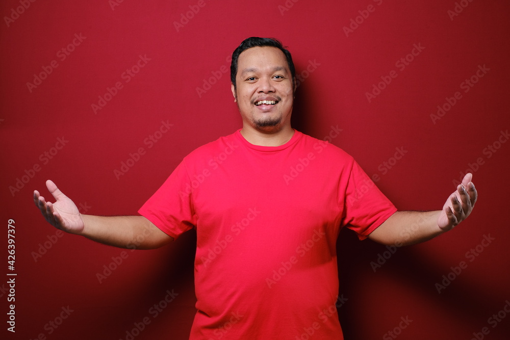 Excited surprised handsome young Asian man in casual red t-shirt doing open hand gesture