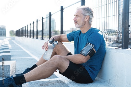 Tired Exhausted Middle-aged Man Resting After Running Outdoors. Handsome Runner Taking Break After Fitness Workout