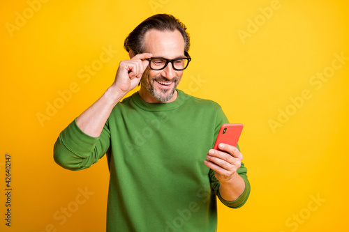 Photo of handsome man hold cellphone look screen adjust specs wear green pullover isolated yellow color background