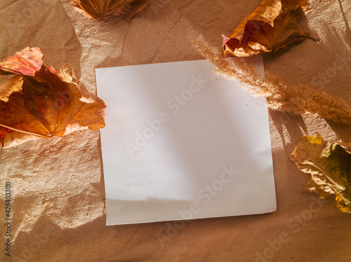 Dry orange-red maple leaves around a white square sheet of paper on a beige mint and textured linen surface. Authenticity concept. Sustainability concept. Mock-up
