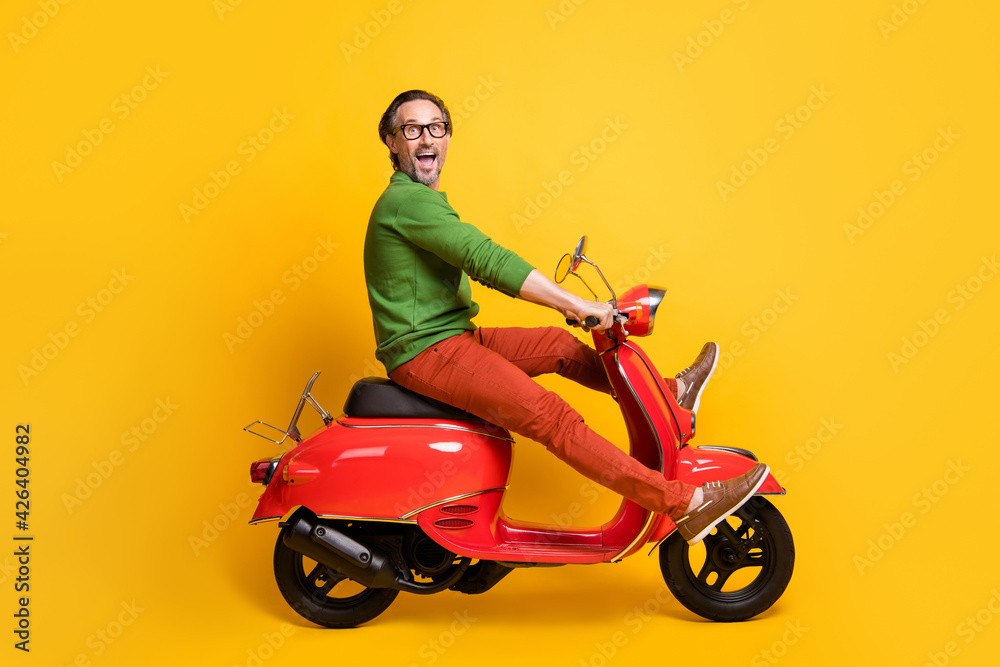 Photo of careless guy ride motorcycle have fun wear specs green sweater trousers footwear isolated yellow color background Photo of careless guy ride motorcycle have fun wear specs green sweater trousers footwear isolated yellow color background