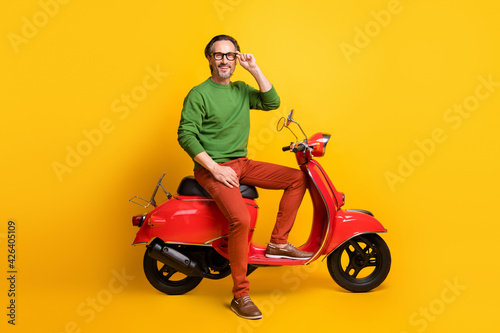 Photo of bearded man ride scooter look camera wear glasses green sweater pants shoes isolated yellow color background © deagreez