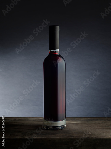 A bottle of red wine, on a wooden empty tabletop against a dark wall background. Wine bottle mockup.