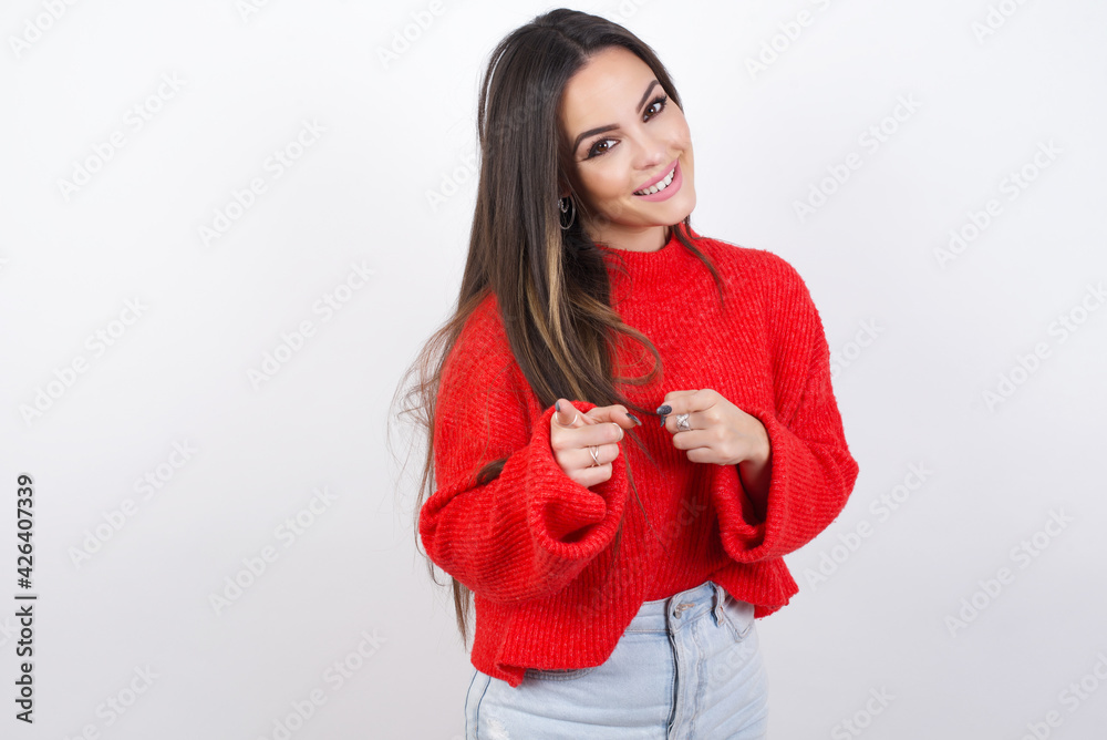 Happy cheerful smiling young beautiful brunette woman wearing red knitted sweater over white wall looking and pointing aside with hand. Copy space and advertisement concept. Happy cheerful smiling young beautiful brunette woman wearing red knitted sweater over white wall looking and pointing aside with hand. Copy space and advertisement concept.