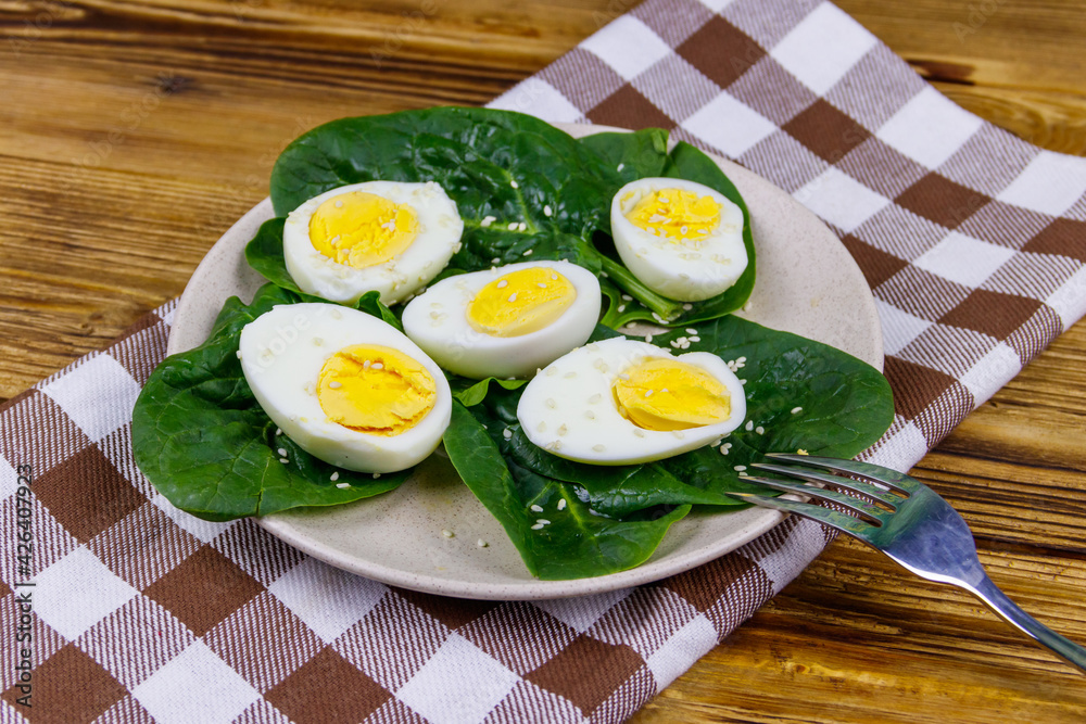 Boiled eggs with fresh spinach leaves and sesame seeds on wooden table Boiled eggs with fresh spinach leaves and sesame seeds on wooden table