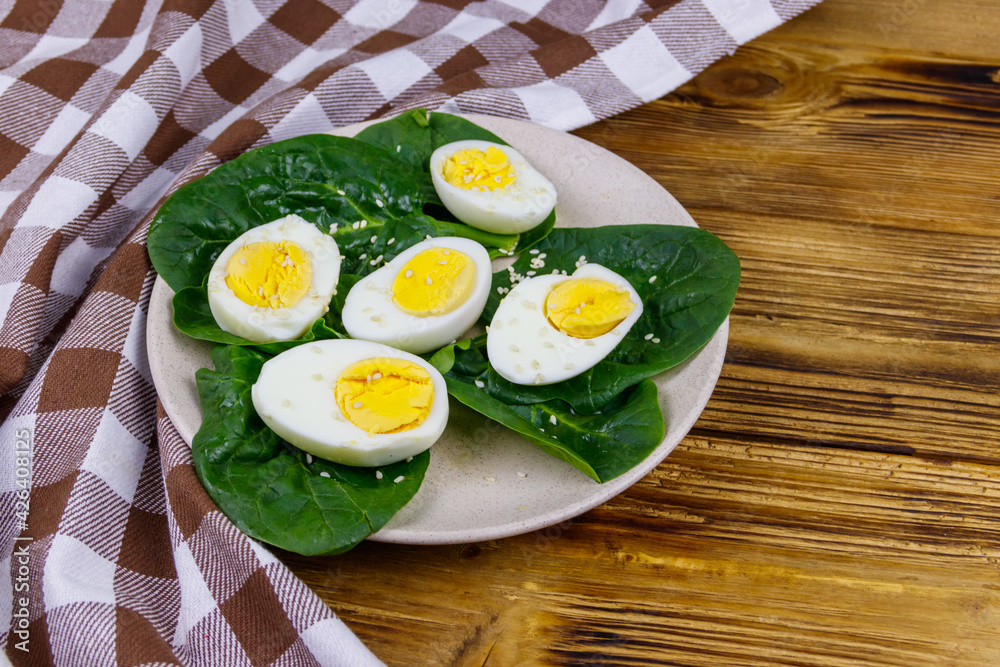 Boiled eggs with fresh spinach leaves and sesame seeds on wooden table Boiled eggs with fresh spinach leaves and sesame seeds on wooden table