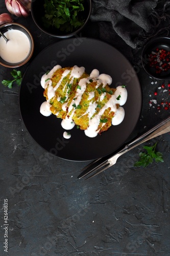 Potato pancakes with zucchini served with sour cream on dark table. Top view with copy space.