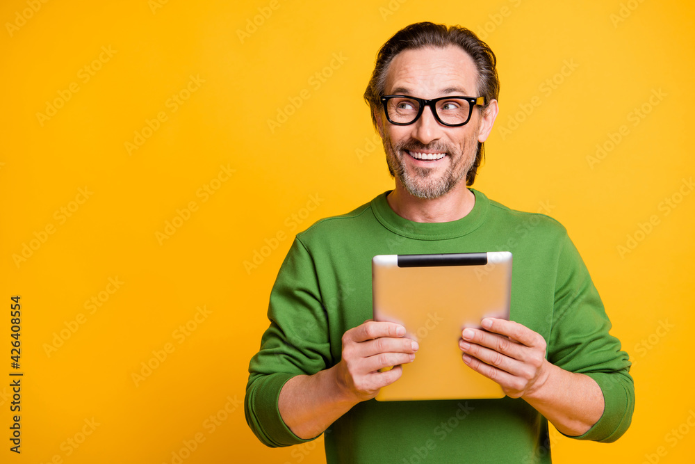 Photo of funny dreamy guy hold tablet look up empty space wear eyewear green sweater isolated yellow color background Photo of funny dreamy guy hold tablet look up empty space wear eyewear green sweater isolated yellow color background