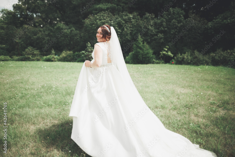 Beautiful brunette bride in elegant white dress holding bouquet posing neat trees Beautiful brunette bride in elegant white dress holding bouquet posing neat trees