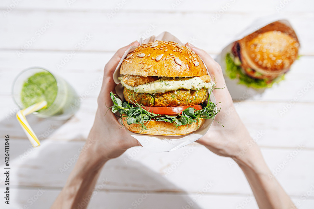 Vegan with a lump, gluten-free, with flax seeds. chickpea burgers with arugula, radish, avocado cucumber and hummus. Plant based diet concept. Burger in the hands of a woman sitting an open-air cafe