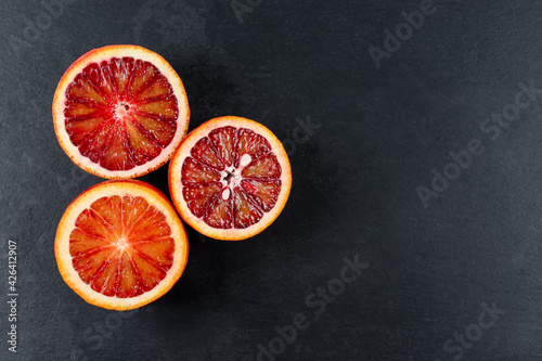 Bloody oranges cut in half on black slate board. Red sicilian orange fruit. Top view, free space for text