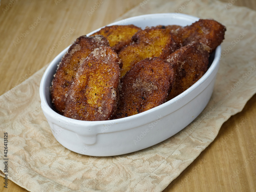 Traditional homemade and Delicious Spanish Torrijas in a ceramic platter on a wooden table and a brown napkin Traditional homemade and Delicious Spanish Torrijas in a ceramic platter on a wooden table and a brown napkin