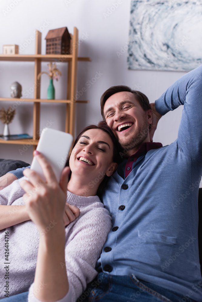 Cheerful man sitting near wife with cellphone on blurred foreground Cheerful man sitting near wife with cellphone on blurred foreground