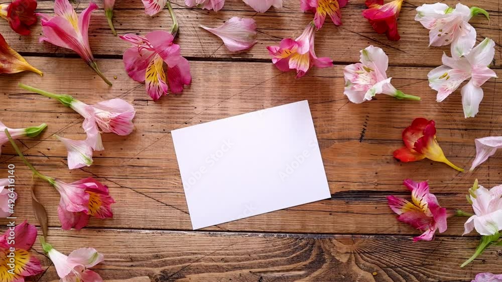 Blank card on a wooden table between flowers top view 