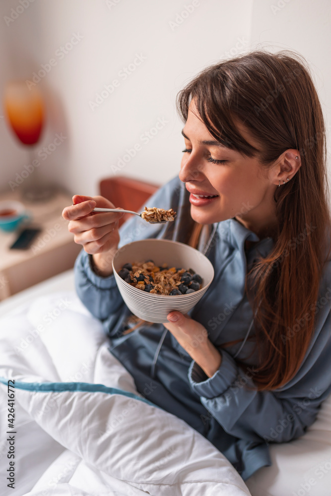 Woman eating cereal while having breakfast in bed