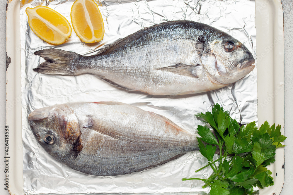 Raw dorado fish with lemon and parsley in a dish on the table. Top View Raw dorado fish with lemon and parsley in a dish on the table. Top View