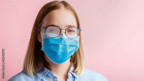 Foggy glasses wearing on woman. Woman portrait in medical protective face mask and eyeglasses wipes blurred foggy misted glasses on pink color background. Covid coronavirus lockdown. Long web banner