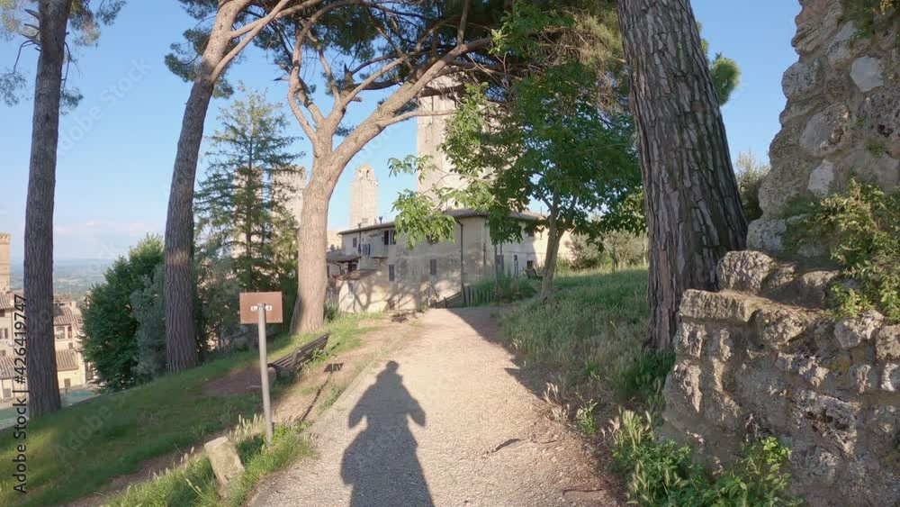 San Gimignano, Tuscany, Italy, slow motion of a walking shadow of a man and a child sitting in the shoulders in direction of the famous landscape of ancient towers in town