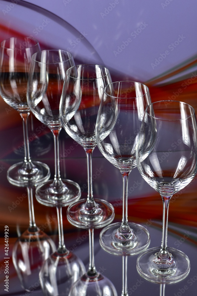 Diagonal of five empty wine glasses on a colored abstract background and reflective surface