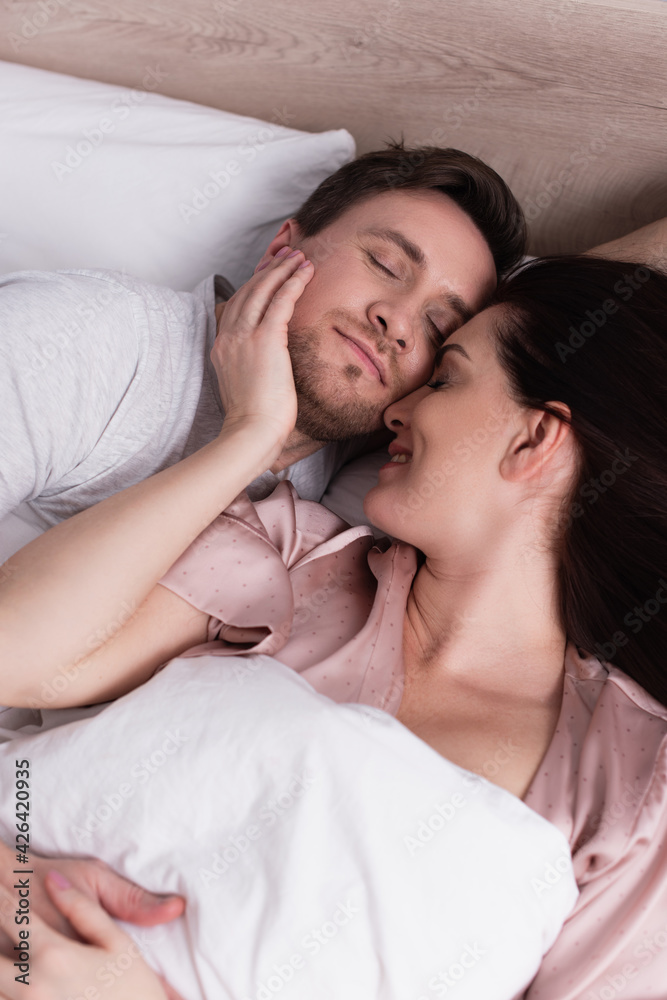 Smiling woman touching face of sleeping husband on bed Smiling woman touching face of sleeping husband on bed