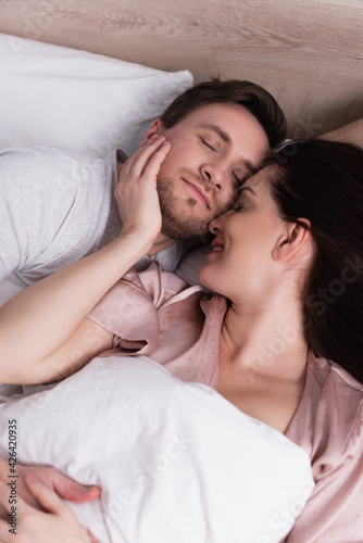 Smiling woman touching face of sleeping husband on bed