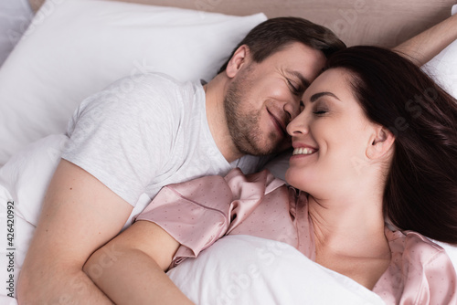 Top view of woman smiling near husband on white bedding
