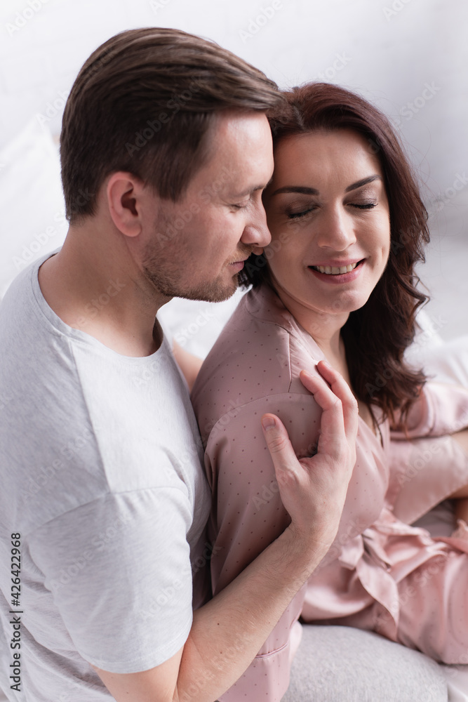 High angle view of man hugging positive wife in pajama on bed High angle view of man hugging positive wife in pajama on bed